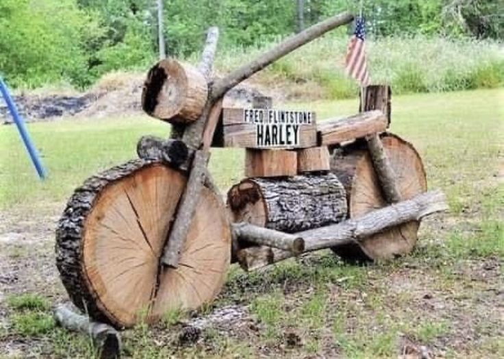 a wooden motorcycle made out of logs in the grass with an american flag on it