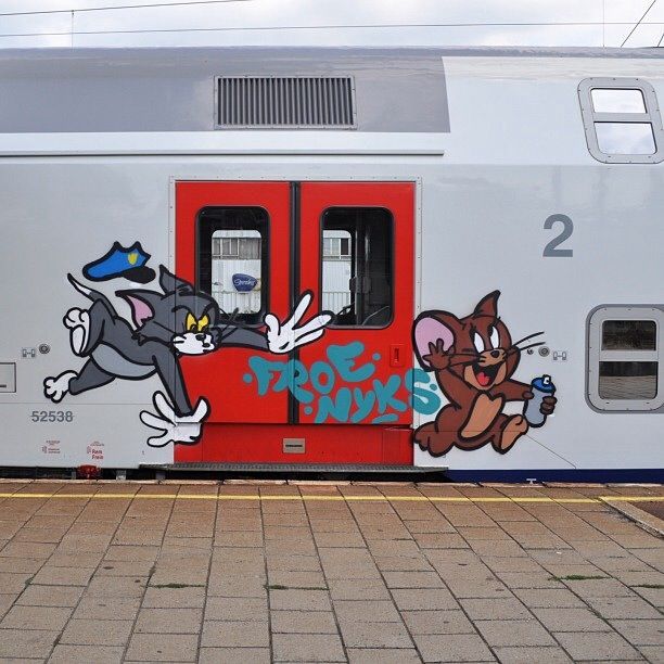 a train with graffiti painted on it's side next to a brick walkway and sidewalk