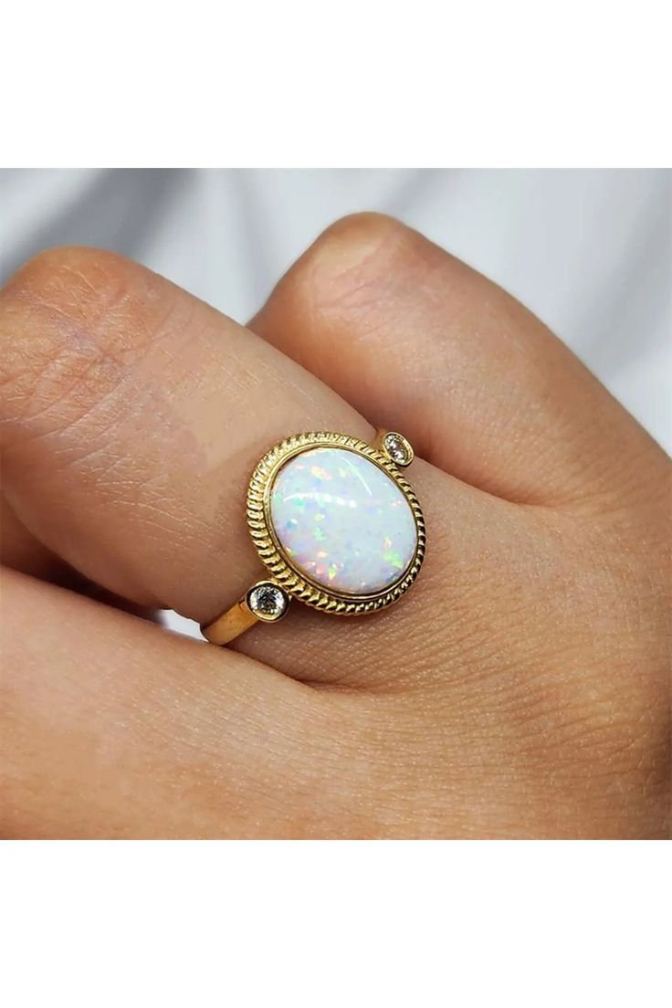 a woman's hand holding a ring with an opal stone in the middle