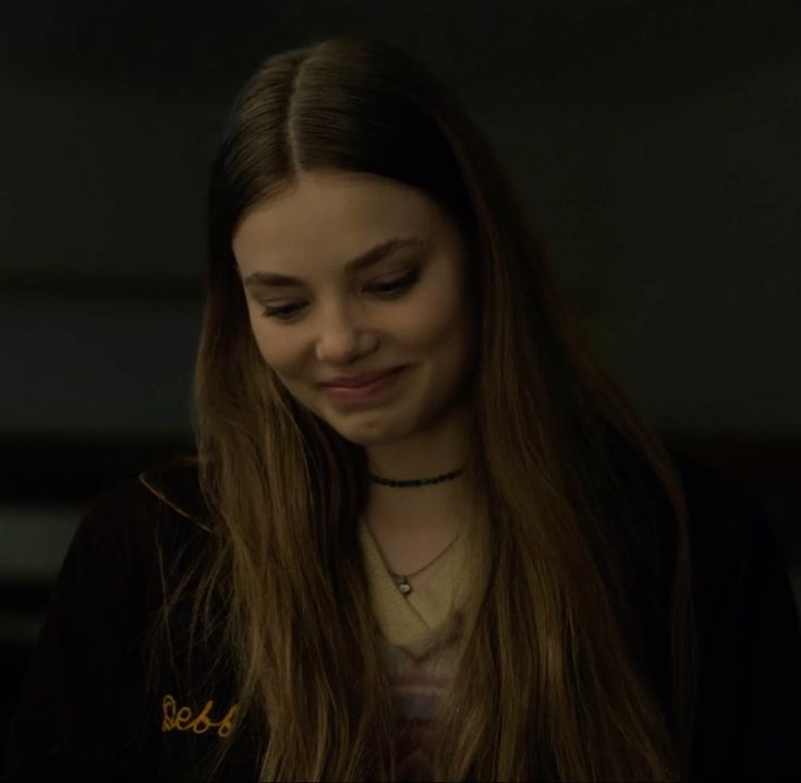 a young woman with long hair looking down at her cell phone in the dark room