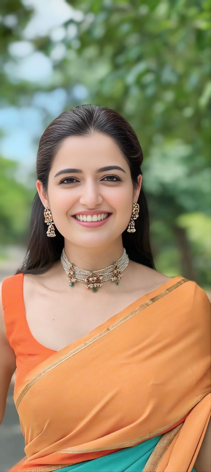 a woman in an orange and blue sari smiles at the camera with trees in the background