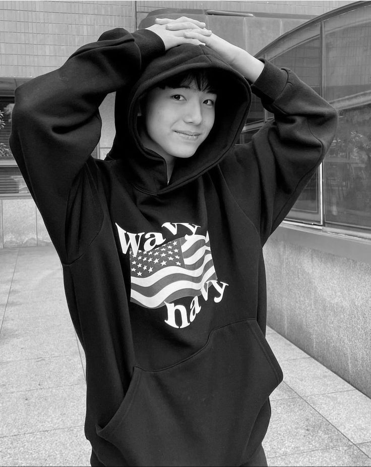 a woman in a black hoodie is standing on the sidewalk with her hands behind her head