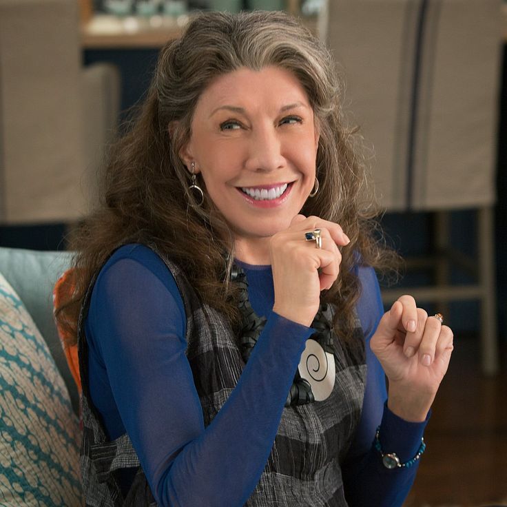 a woman sitting on a couch smiling at the camera with her hand under her chin