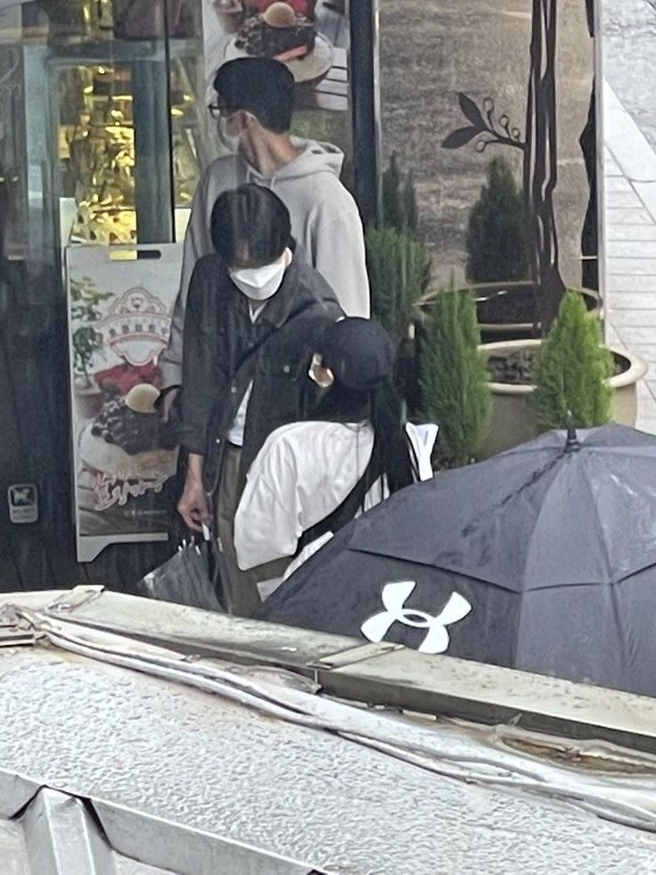 two people walking in the rain with umbrellas and other items on display behind them