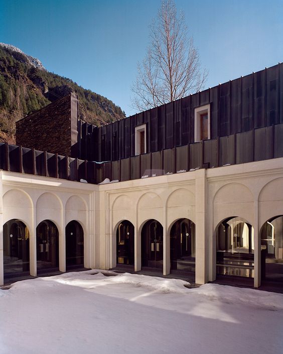 an empty courtyard in front of a building with arched doorways and black roofing