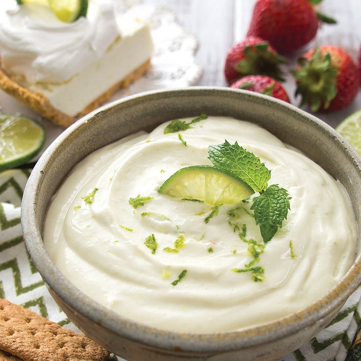 a bowl filled with white sauce next to crackers and strawberries