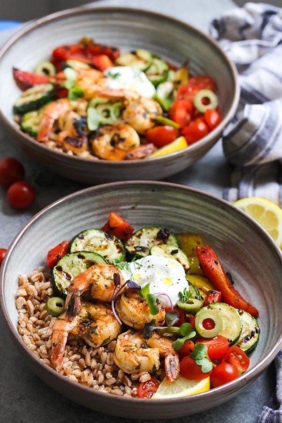 two bowls filled with shrimp, rice and veggies next to lemon wedges