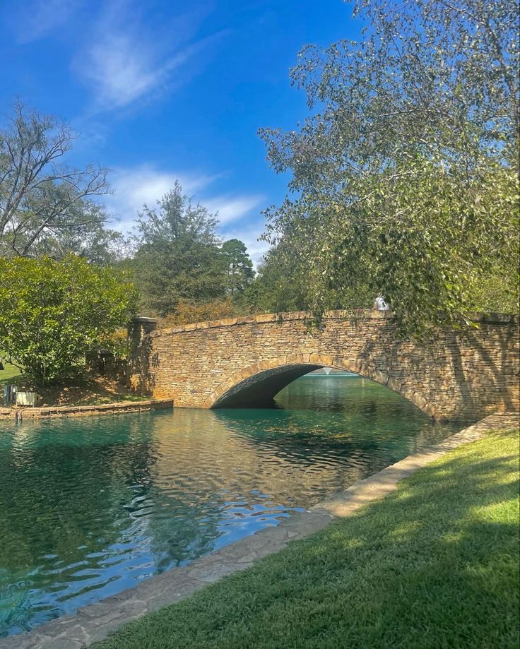 a stone bridge over a body of water next to a lush green field and trees