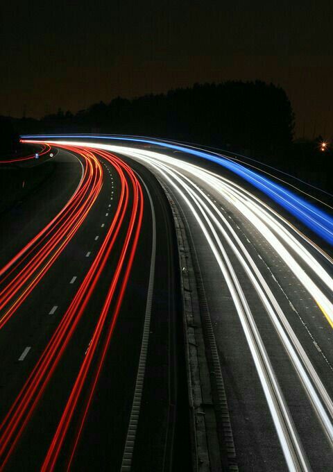 long exposure photograph of highway at night with light streaks on the road and trees in the background