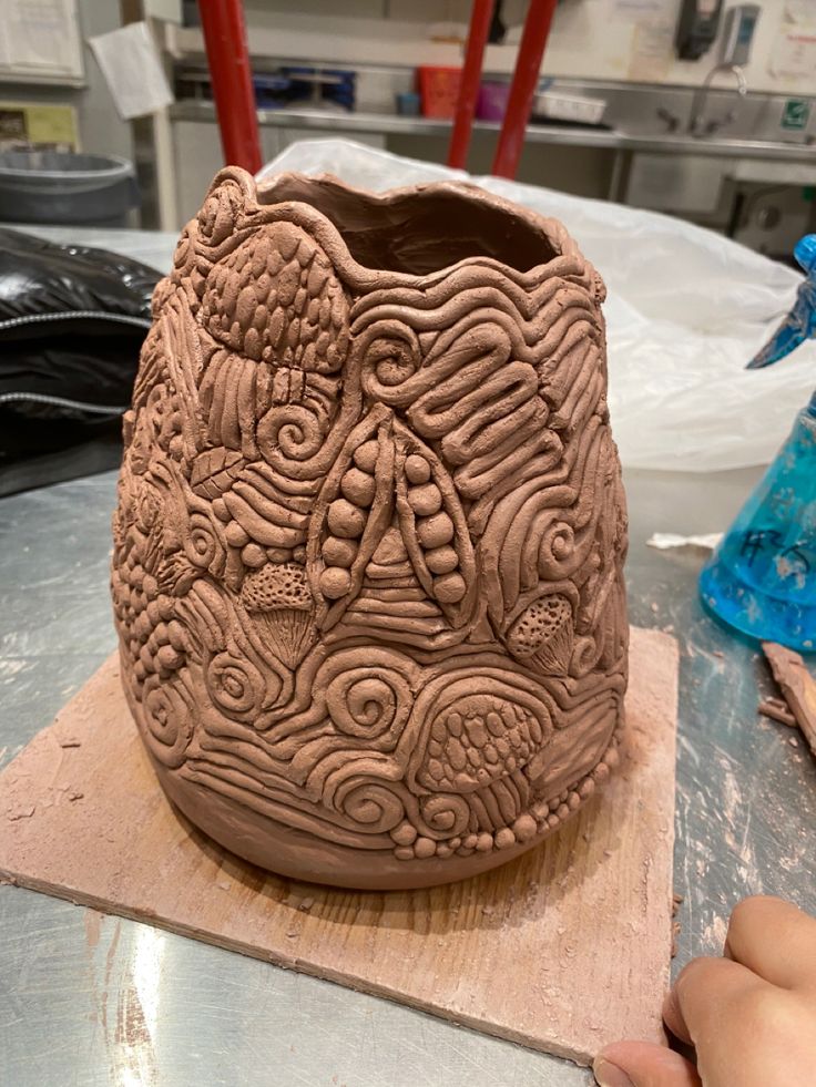 a clay vase sitting on top of a wooden table next to a person's hand