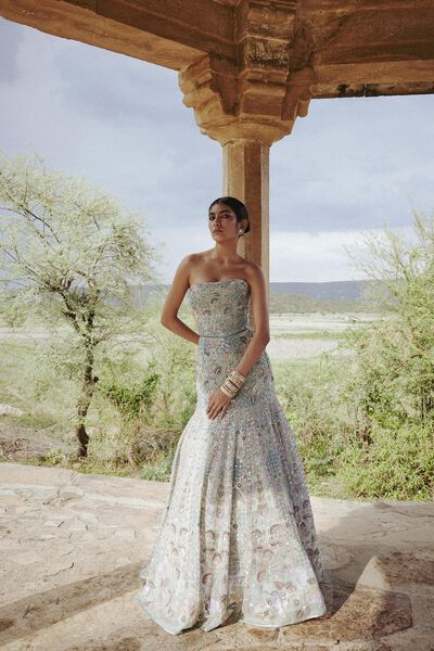 a woman standing under a wooden structure wearing a dress with flowers on the bottom and side