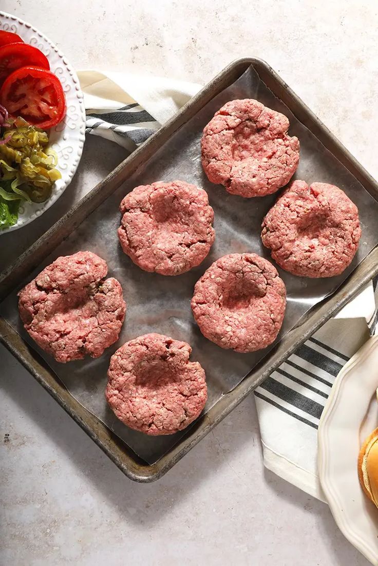 some hamburgers are on a tray next to a bowl of salad and a plate of tomatoes