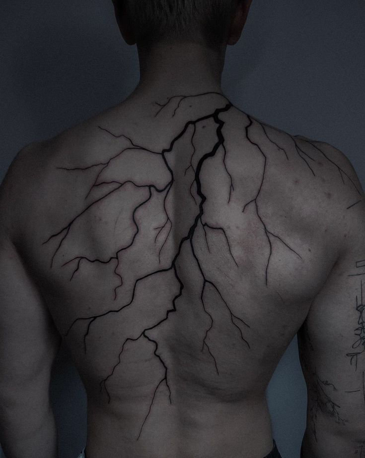 the back of a man with tattoos on his upper and lower torso, showing lightning