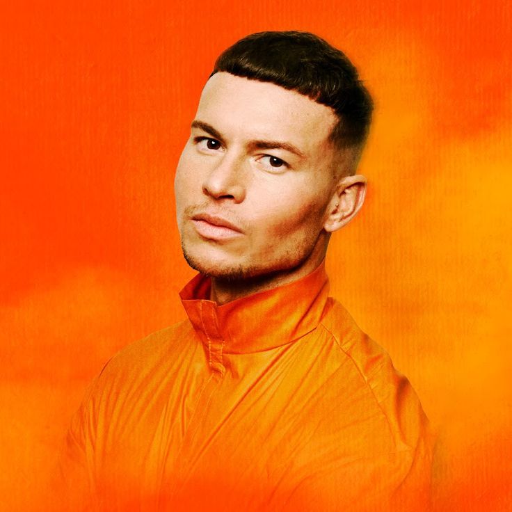 a man in an orange shirt is looking at the camera and has his head tilted to the side