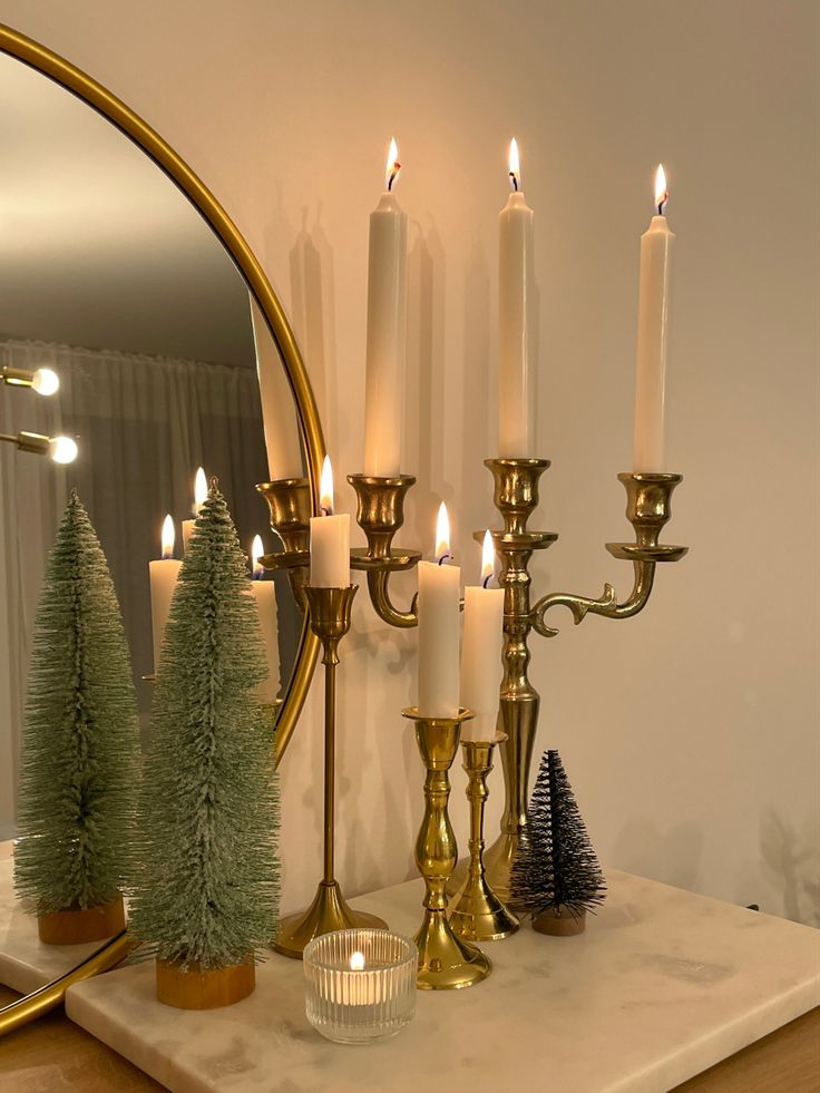 candles and christmas trees are on a mantle in front of a mirror with a gold candle holder