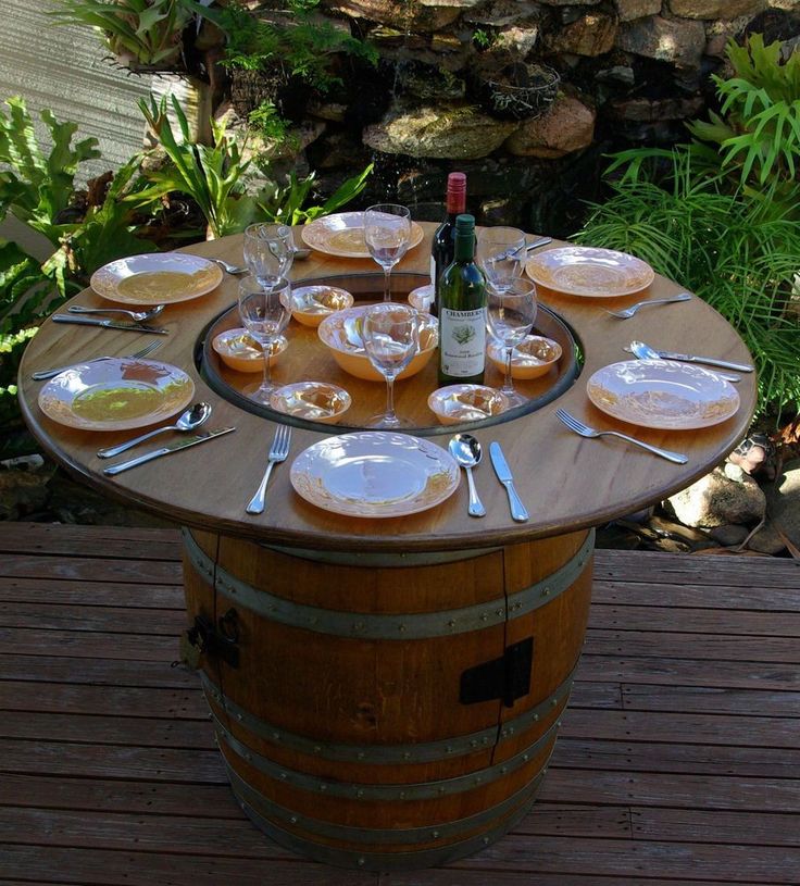 a wine barrel table with plates and glasses on it in the middle of a garden