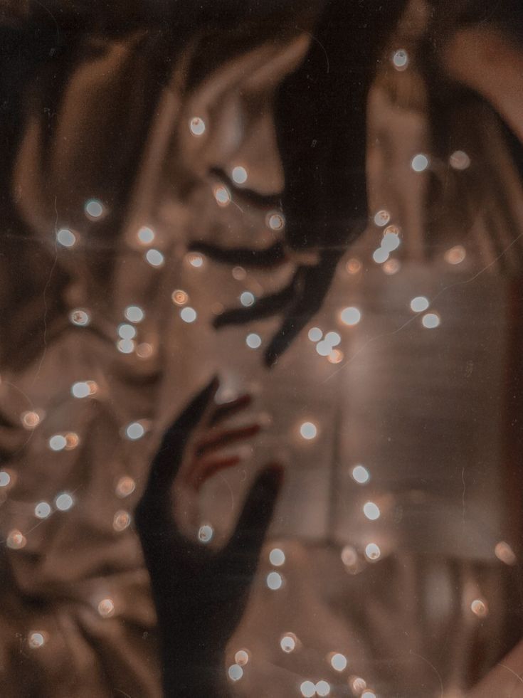 the reflection of a woman's hand in a mirror with lights behind her and hands reaching out