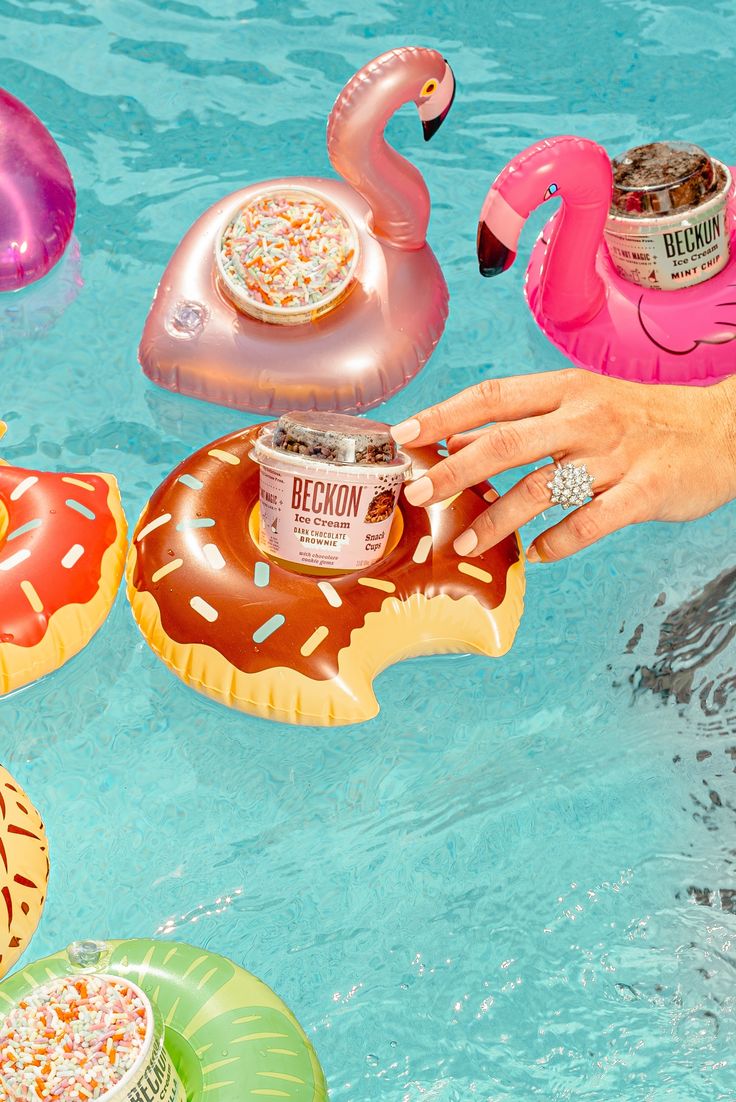 a person holding an ice cream in their hand next to pool floats and flamingos