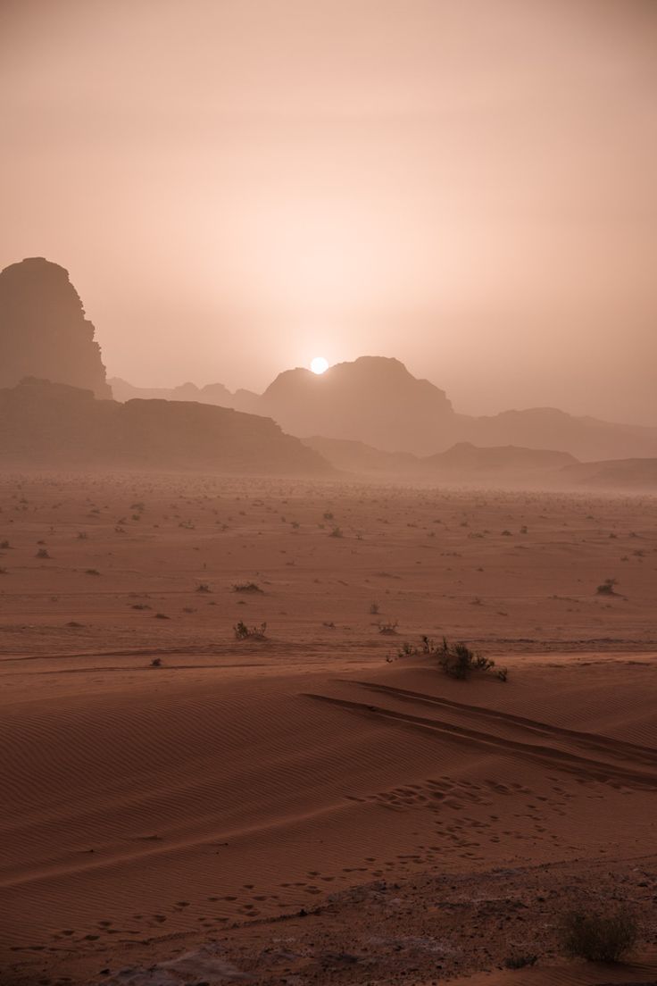 the sun is setting in the desert with sand dunes and rocks on either side,