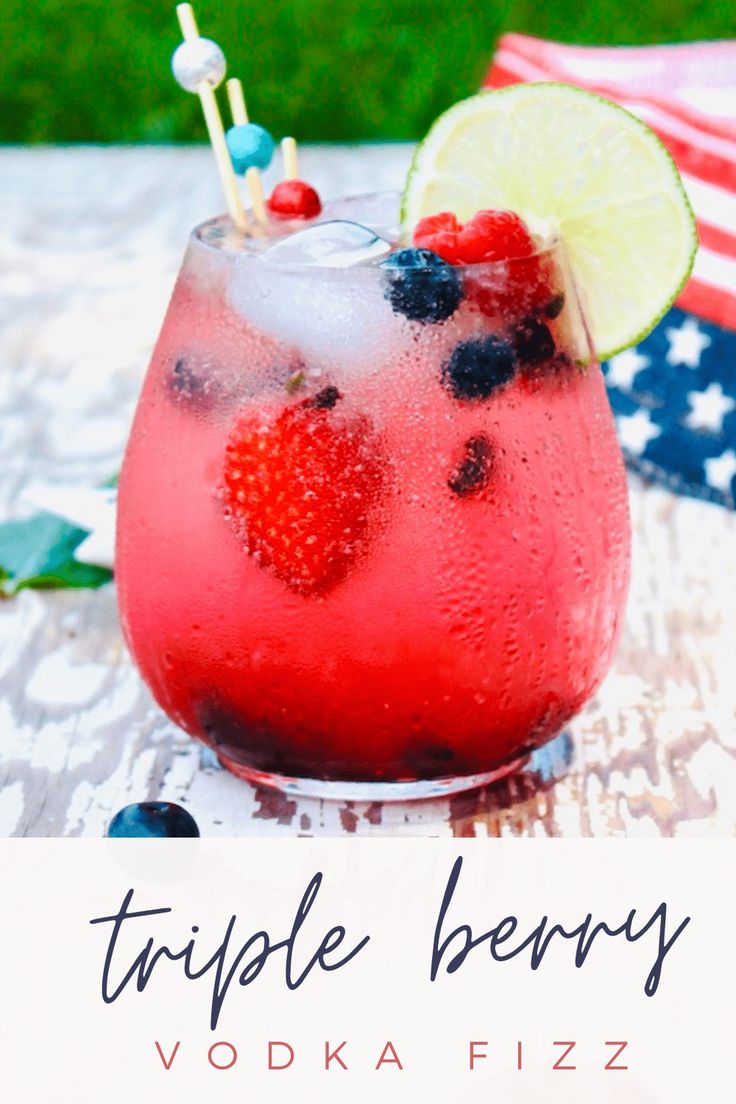 a drink in a glass with strawberries, blueberries and lime on the side