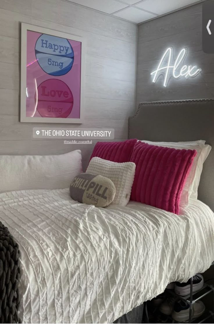 a bed with white sheets and pink pillows in a room that has a neon sign on the wall above it