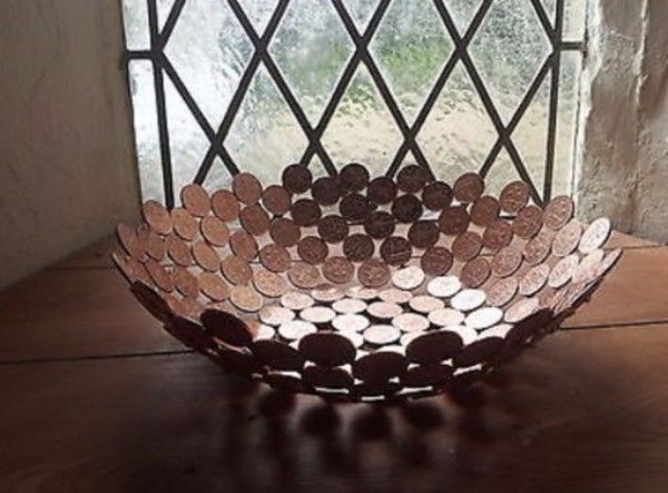 a metal bowl sitting on top of a wooden table next to a window with coins in it