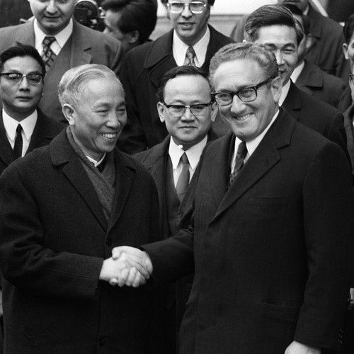 black and white photograph of two men shaking hands with other men in suits behind them