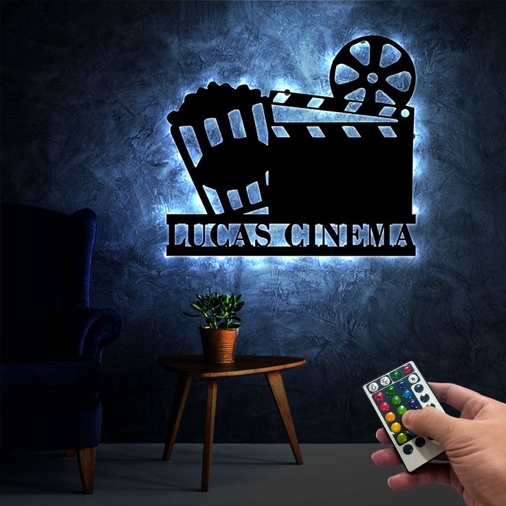 a hand holding a remote control in front of a wall with a movie logo on it