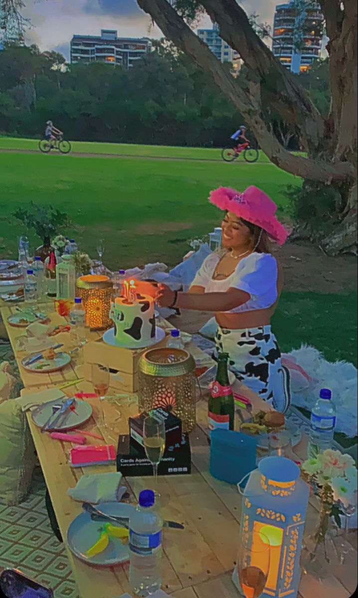 a group of people sitting at a picnic table with plates and cups on it in the park