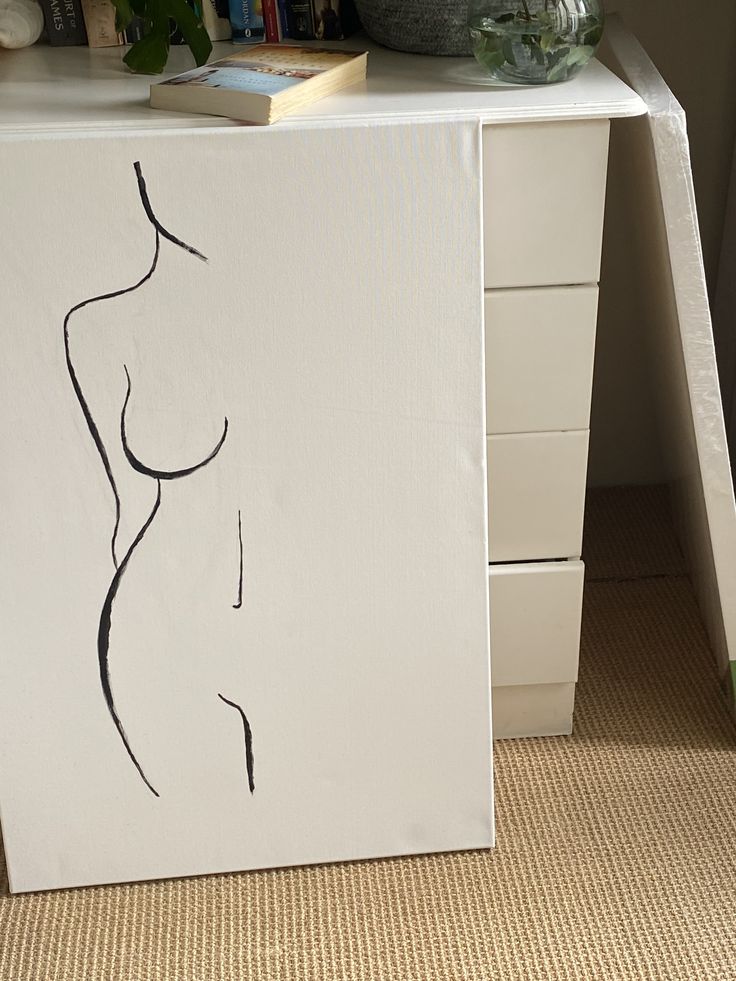 a white box with a drawing of a woman's torso on it next to a plant