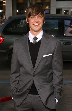 a man in a suit and tie standing next to a car at a red carpet event