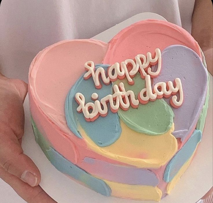 a person holding a heart shaped cake with the words happy birthday written in frosting