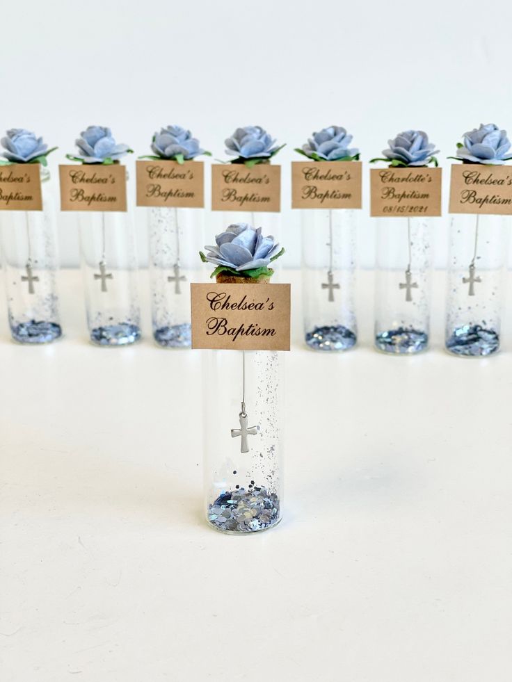 there are many small glass vases with flowers in them and name tags attached to the bottles