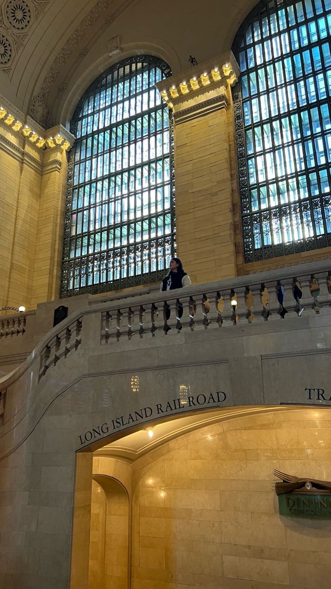 the inside of a train station with two people sitting on the railings and windows