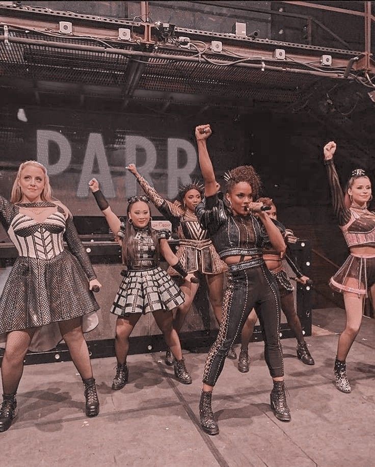 the girls are performing on stage in costumes and boots with their hands up to the air