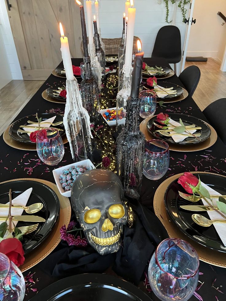 a table set with black and gold plates, silverware, candles and skulls on them