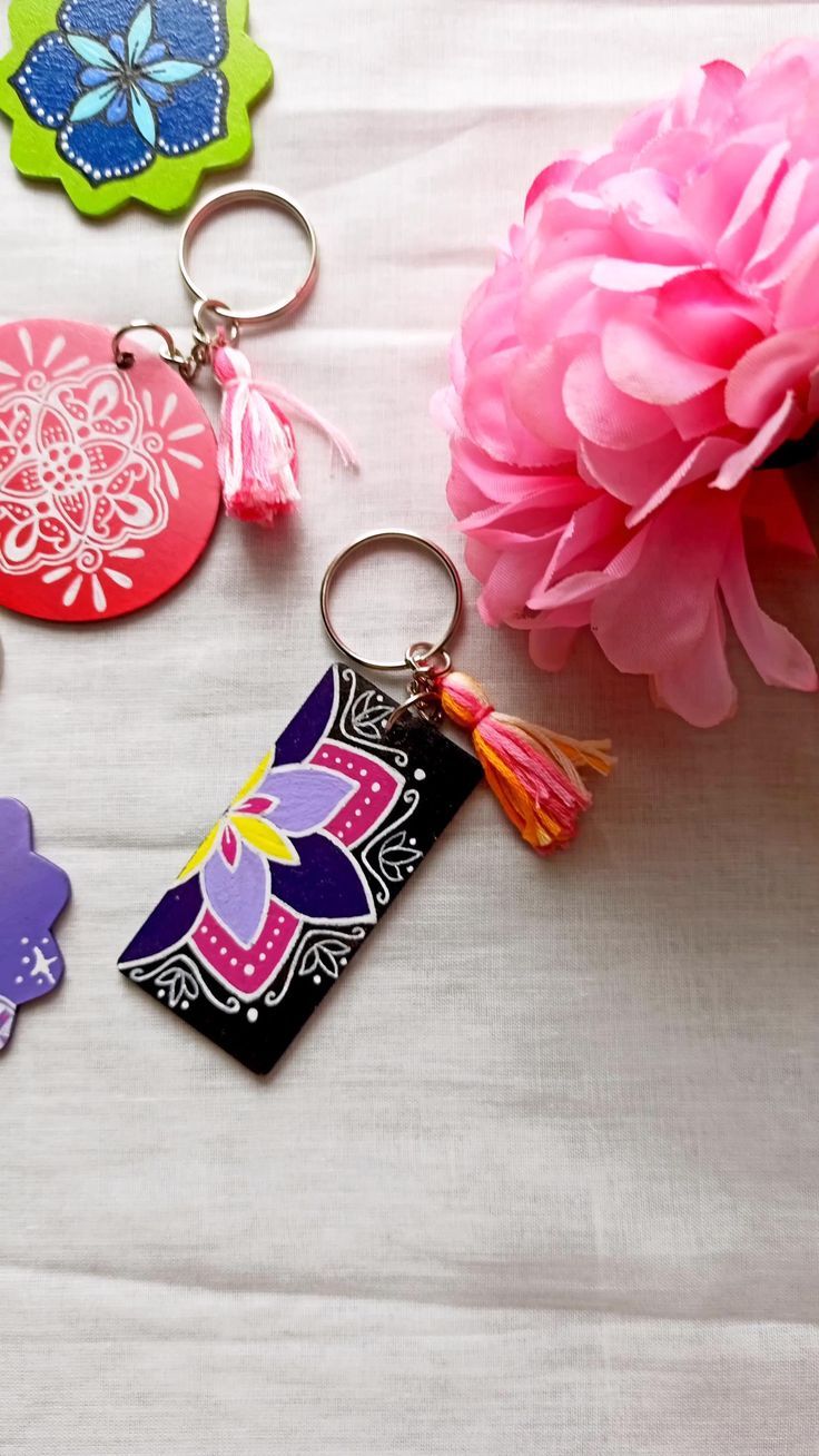 four different colored tags with tassels next to a pink flower on a white surface