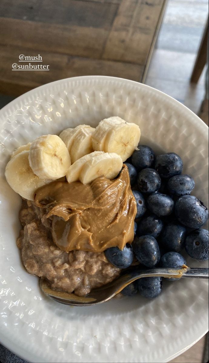 a white bowl filled with oatmeal and bananas on top of blueberries