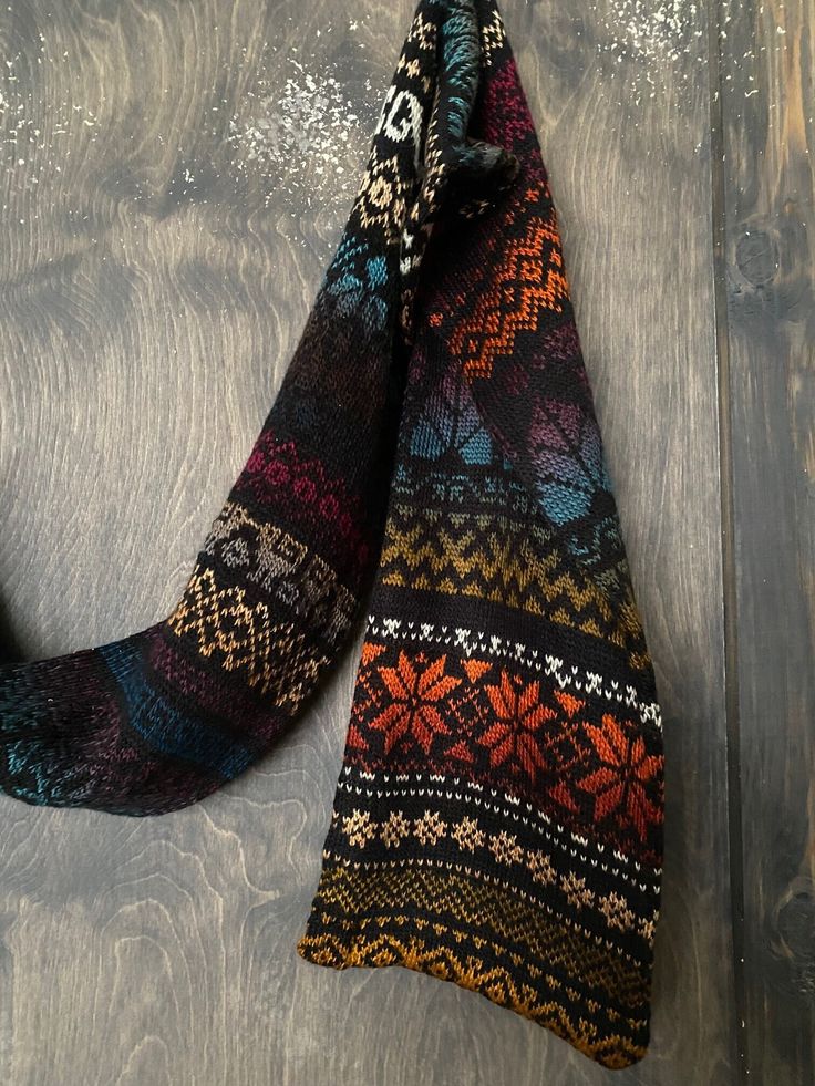 a multicolored scarf hanging from a hook on a wooden door with snowflakes in the background