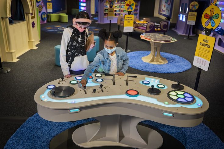 two people standing in front of a table with electronic devices on it and blue carpet