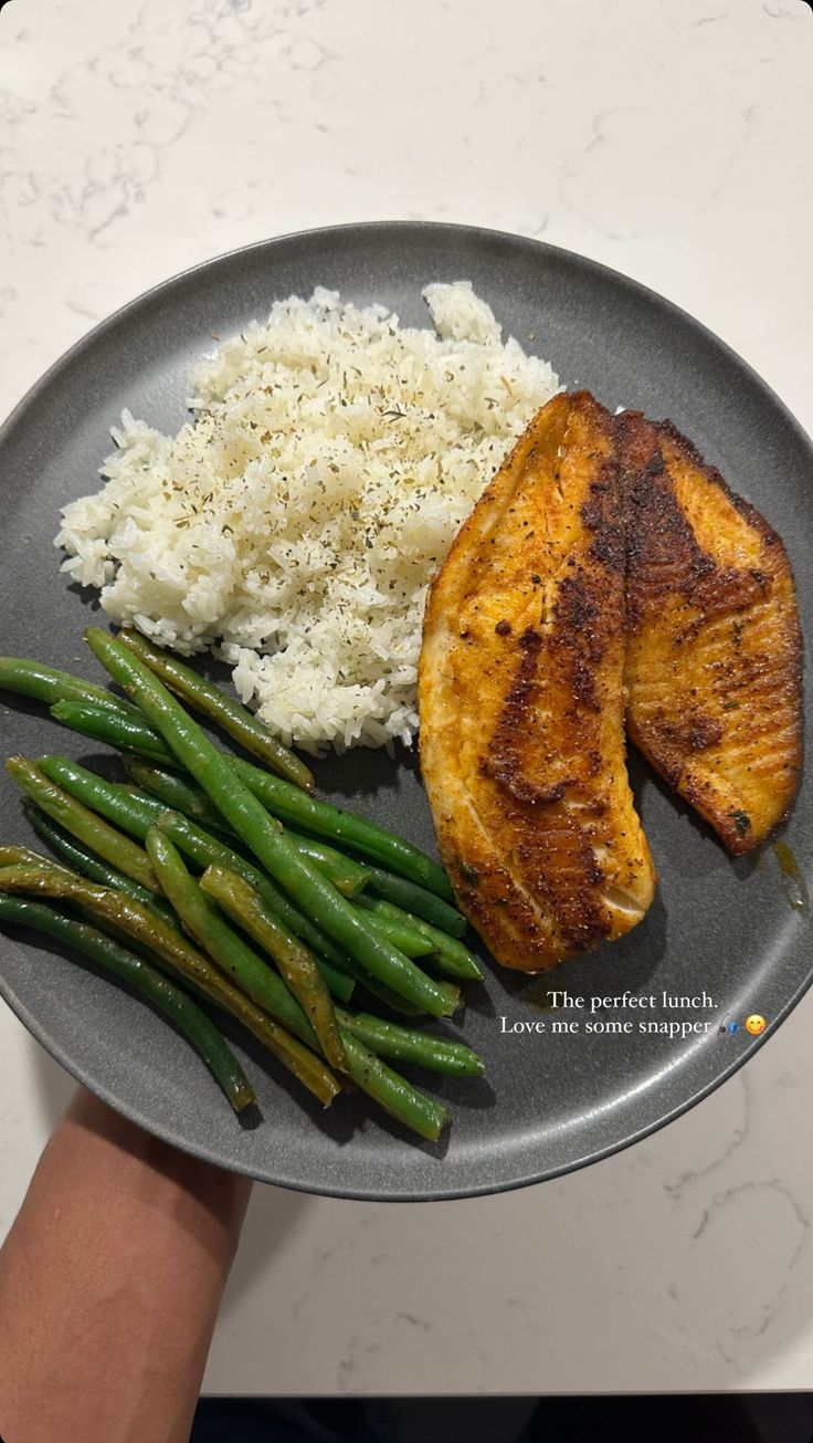 a plate with rice, green beans and chicken on it is being held by a person