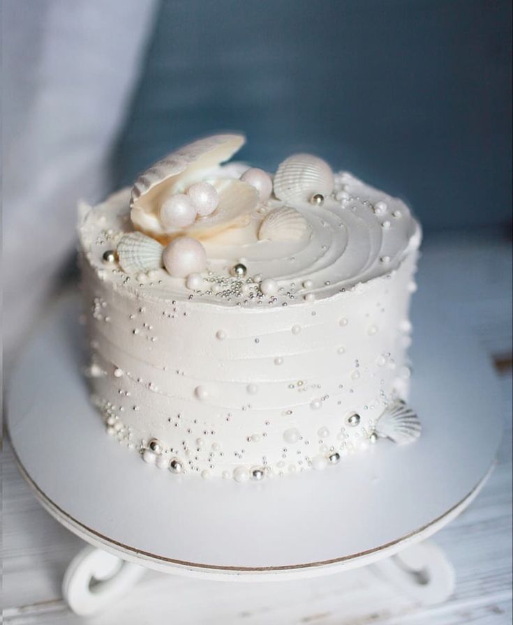 a white cake with pearls and seashells on it's top is sitting on a plate