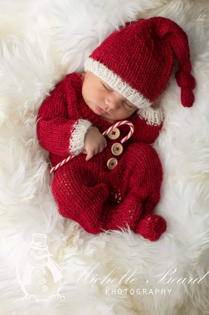 a newborn baby wearing a red knitted christmas outfit and hat laying on white fur