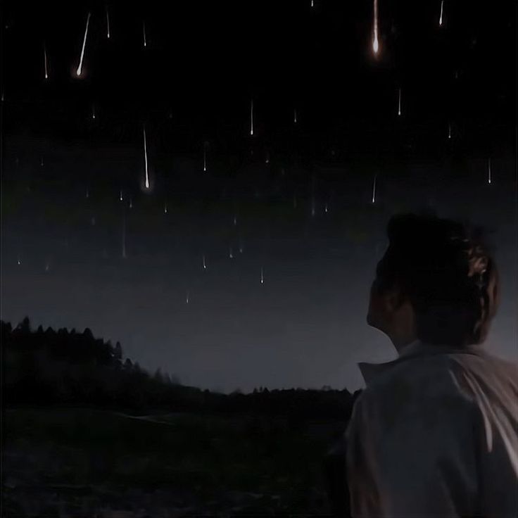 a man standing in front of a dark sky filled with stars and shooting comets