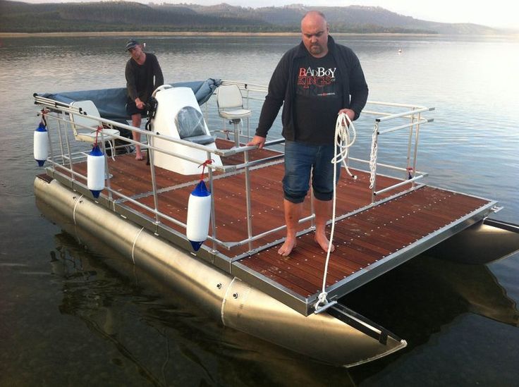 two men are standing on the deck of a pontoon boat in the water while another man stands next to it