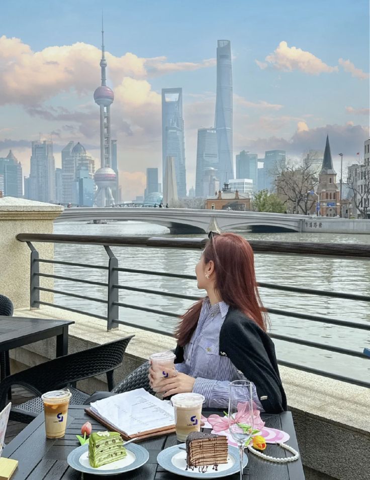 two women sitting at an outdoor table with food and drinks in front of the city skyline