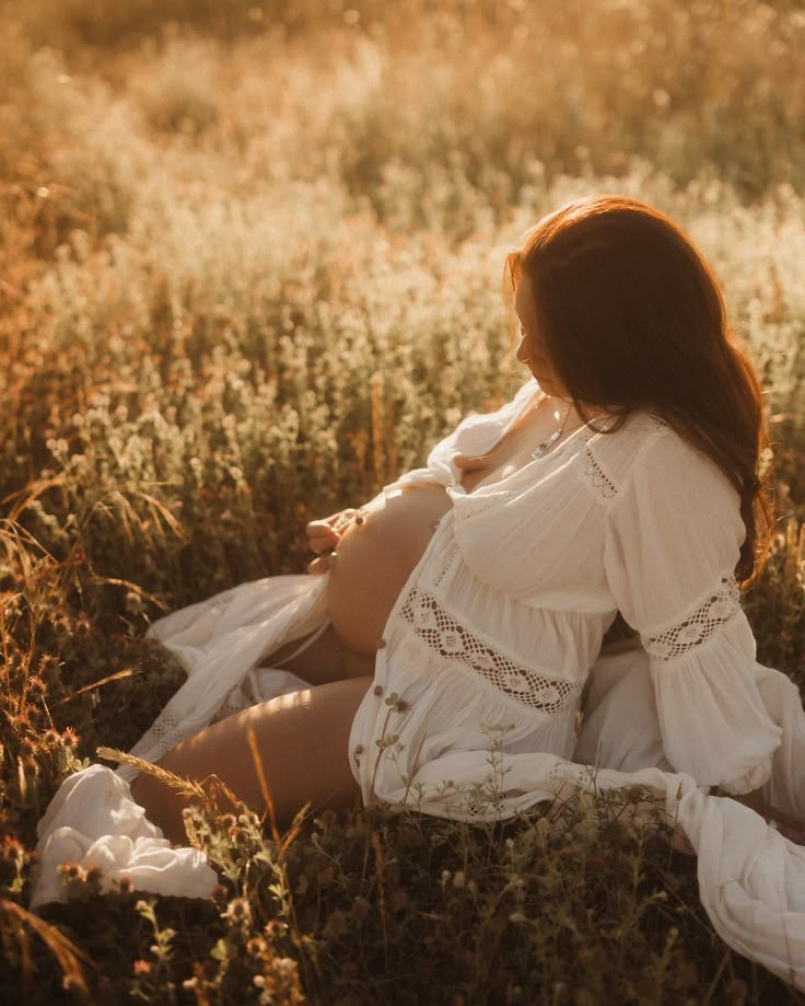 a woman sitting in the middle of a field wearing a white dress and holding her hands behind her back