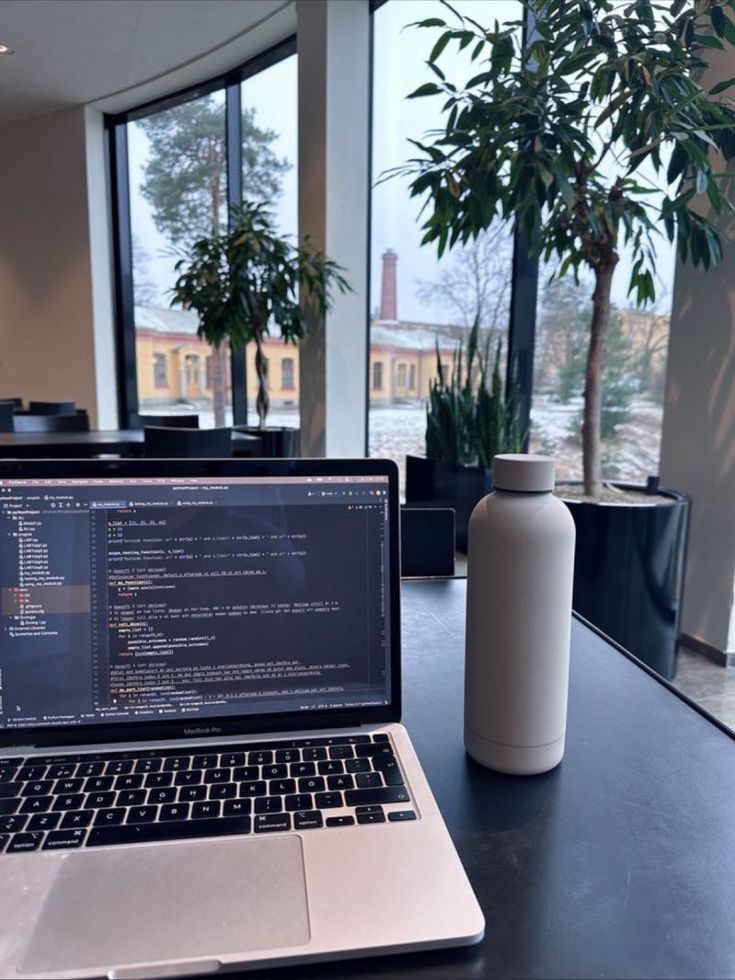 an open laptop computer sitting on top of a table next to a vase and potted plant