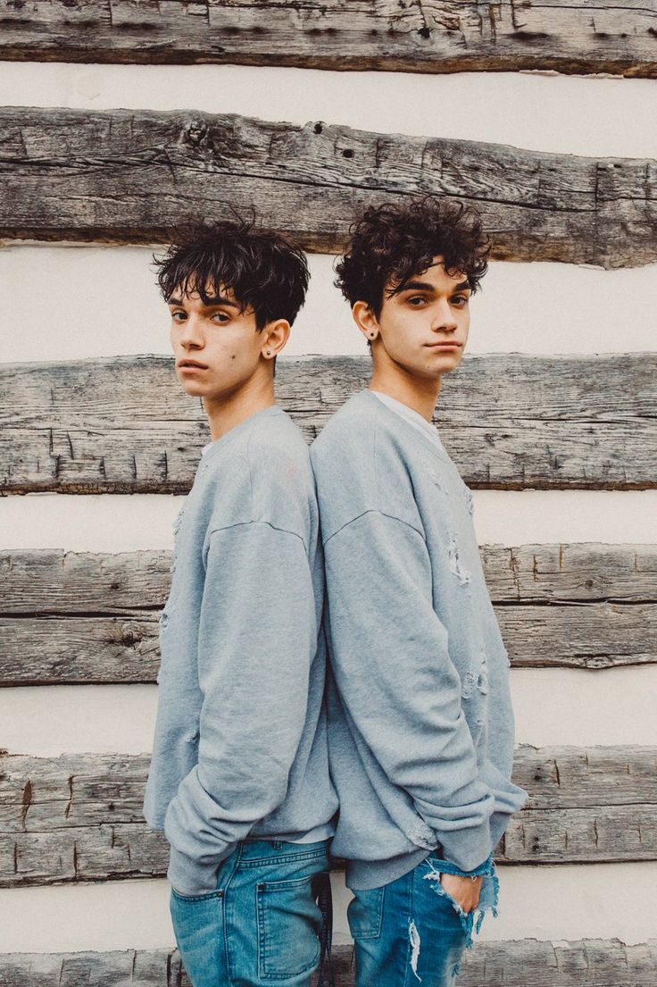 two young men standing next to each other in front of a wooden wall with logs