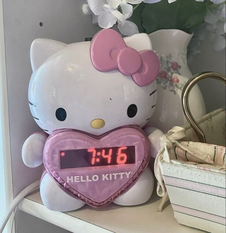 a hello kitty alarm clock sitting on top of a shelf next to a vase with flowers